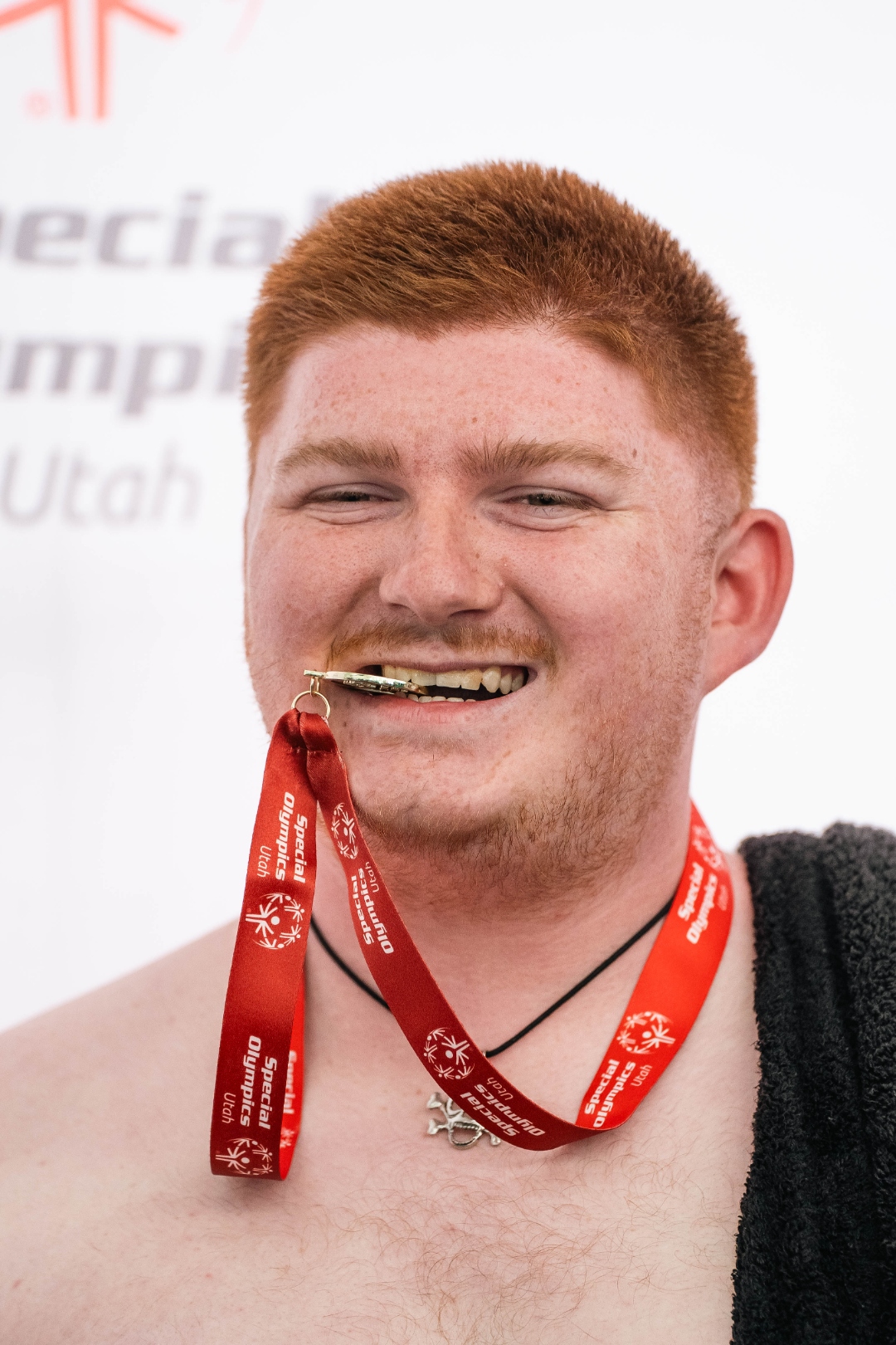 Client grinning ear to ear while biting his Special Olympics Utah medal