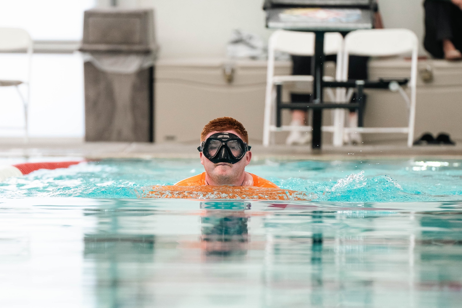 Client in orange shirt and goggles swimming mid-race at the Special Olympics swim meet