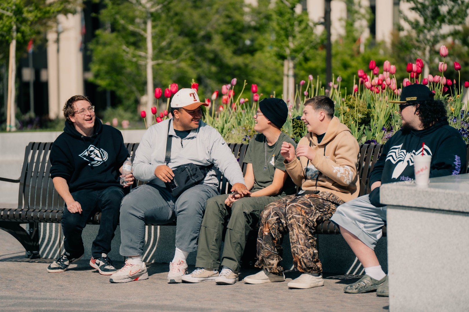 FaleOfaz clients and staff laughing together on a bench surrounded by tulips during a community outing